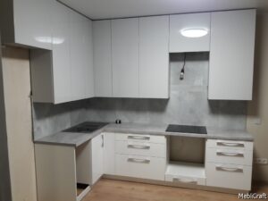 Кутова кухня в сіро-білих тонах з глянцевими фасадами без ручок, фасад звисає нижче за корпус